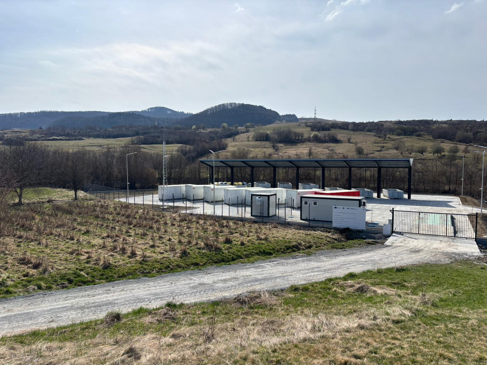 Vedere a Centrului de Colectare prin Aport Voluntar din Eremitu, cu poarta de acces și containerele sub copertina metalică